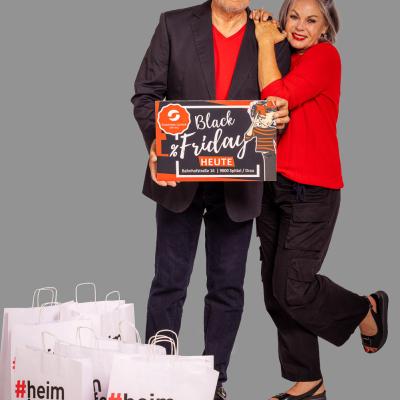 Ein Mann und eine Frau stehen nebeneinander und haben ein Schild mit Black Friday im Stadtparkcenter Spittal an der Hand. Davor stehen Tüten mit dem Aufgdruck #heimkaufen