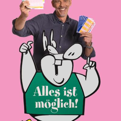 Ein Mann steht vor dem Lottosscheinaufsteller mit Alles ist möglich Lotto - Aufschrift und er hält viele Lottoscheine in der Hand