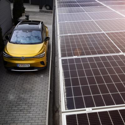 Ein gelber VW ID4 steht in einer Einfahrt. Man sieht von der Vogelperspektive daneben Solarpanele.