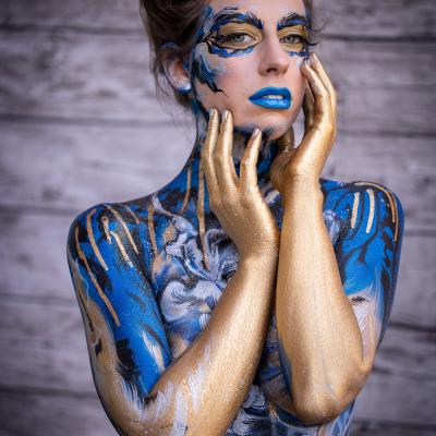 kunstvoll blau bemalte Frau hält sich ihr Gesicht mit ihren Händen 