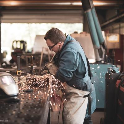 Mann in Werkstatt steht vor Werkbank und Schleift Metall das die Funken sprühen
