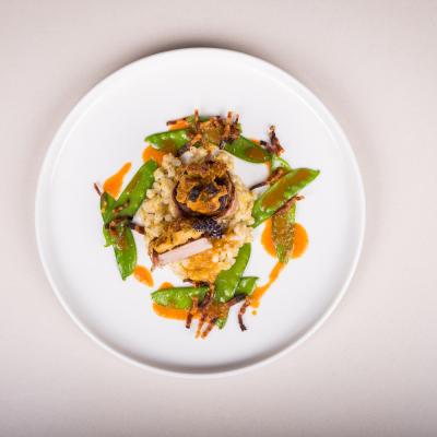 Fleisch auf Reis mit flachen Bohnen als Deko und oranger Sauce auf weissem Teller